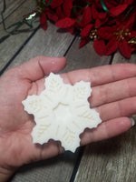 A white soap bar shaped as a snowflake in a hand to represent size which is 2 3/4 x 2 3/4 on the face of the soap